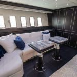 Httpswww Andyquinones Net luxurious lounge inside a private vehicle with a white sectional sofa blue pillows and marble topped tables amid dark wood paneling