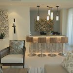 Httpswww Andyquinones Net open plan living area with a marble bar island and five wooden bar stools under pendant lights in a bright neutral space