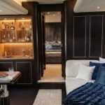 Httpswww Andyquinones Net luxurious hotel suite living area with a glass front liquor cabinet dark wood panels and a white sofa with blue cushions