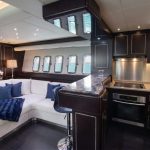 Httpswww Andyquinones Net luxurious yacht salon with white sectional sofa blue cushions dark wood panels and a stainless steel galley to the right