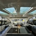 Httpswww Andyquinones Net luxurious yacht interior with a long central seating area and large skylights overhead overlooking a marina