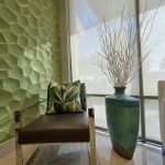 Corporate office accessorizing - https://www.andyquinones.net Httpswww Andyquinones Net modern interior seating area brown leather chair with a green geometric cushion beside a teal ceramic vase with bare branches and a green honeycomb wall